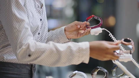 Black woman is comparing two models of smartwatch in electronics shop, holding Stock Footage 153137288