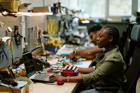 Black Woman Engineer Programming Robotics Hardware with Laptop in Workshop Stock Photos