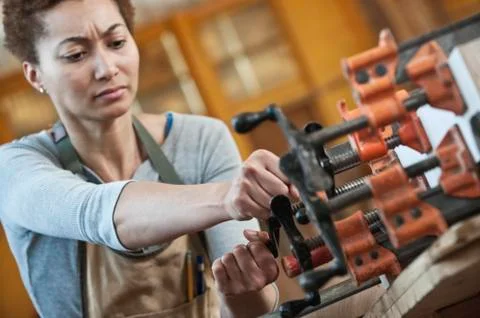 Black woman factory worker adjusting clamps while glueing a large wooden part in Stock Photos
