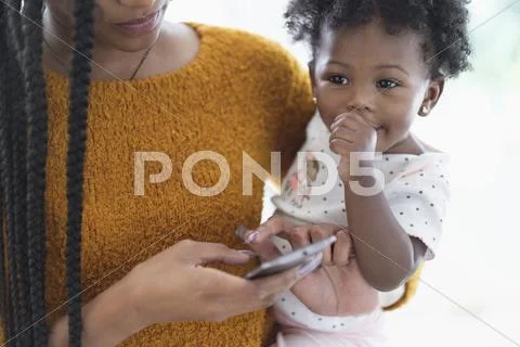 Black Woman Holding Baby Daughter Using Cell Phone