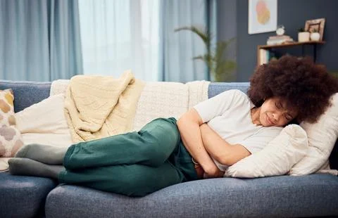Black woman, lying on sofa with stomach, menstruation or pain holding abdomen in Stock Photos