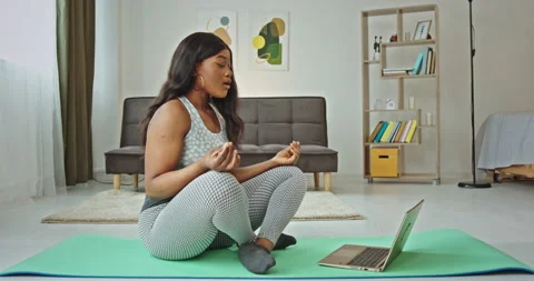 Overweight black woman sitting on sports mat in lotus pose