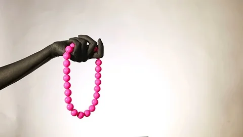 Black woman's hand with pink plastic beads. Fashion jewelry on a black painte Stock Footage 100682471
