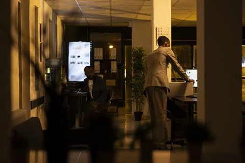 Black worker fired from job packing belongings at desk in dark office Stock Photos