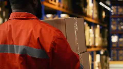 Black worker moving cargo pallets across busy warehouse floor Stock Footage 332911200