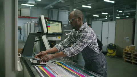 Black Worker Using Spectrophotometer and Operating Machine in Printing House Stock Footage 335483239