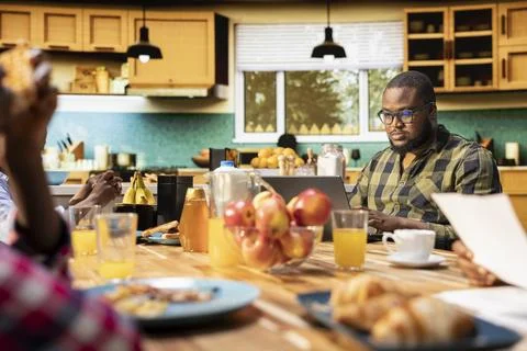 Black working dad on computer ignoring son and family at breakfast table Stock Photos