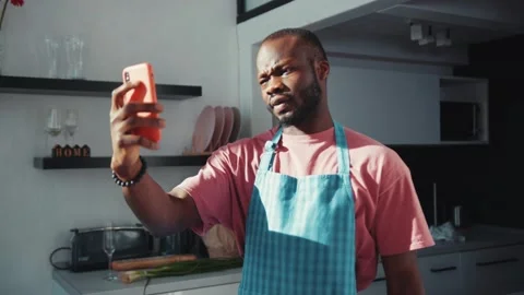 Black young appealing man in apron talking on smartphone online video call Stock Footage 131670106
