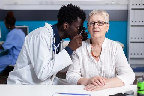 Black young doctor using otoscope on elder patient Stock Photos