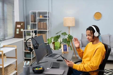 Black young man as software developer using video chat at workplace and waving Stock Photos