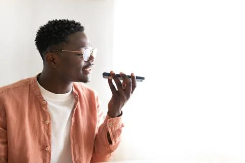 Black young man using mobile phone to send voice message at home. Copy space. Stock Photos