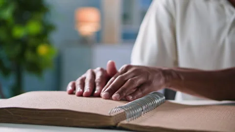 Black young man with vision problems reads book for the blind, moving his Stock Footage 254706963