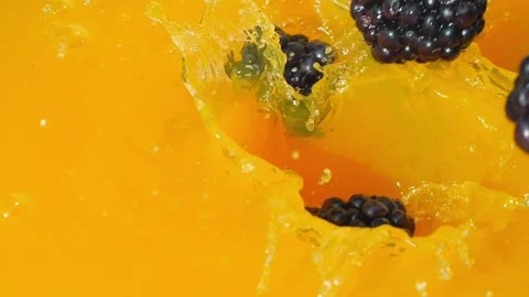 Blackberries splashing into bright orange juice, creating dynamic bubbles Stock-Footage 288114441
