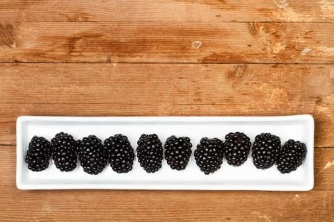 Blackberries on a white rectangular plate on a wooden table in a top view Foto stock