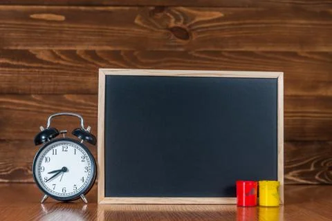 A blackboard with space for text, colored paint and an alarm clock on wooden Stock Photos