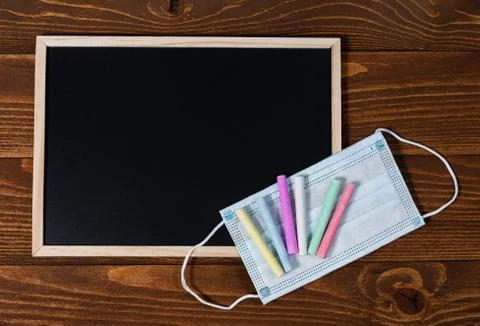 A blackboard with space for text, set of colored crayons and a protective mask Stock Photos