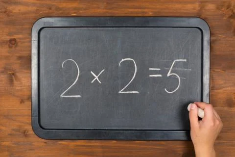Blackboard with wrong maths equation and chalk in hand Stock Photos