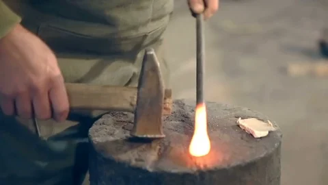 Blacksmith bend hot metal with a hammer on the anvil in the smithy Stockbeeldmateriaal 77006094