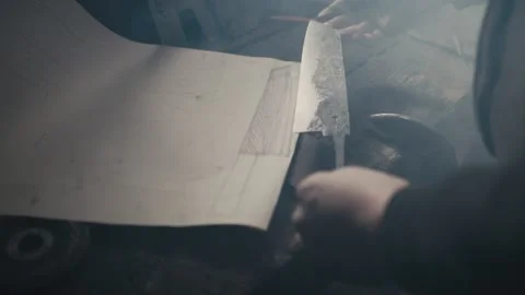Blacksmith checking drawing of a knife blade he is making Stock Footage 131749060