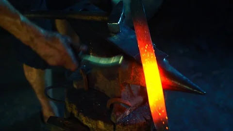 Blacksmith clean off dross from red-hot iron and forge sword on anvil Stock Footage 127882785
