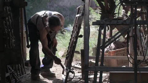 Blacksmith cleaning slag from a grating after welding. Stock Footage 248959085