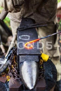 Blacksmith curves iron buckle with hammer on anvil Stock Photos