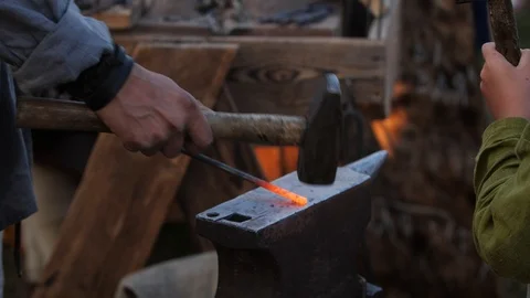 Blacksmith father and son forge hot steel on an anvil by hammer. Making arrow Stock Footage 114928823