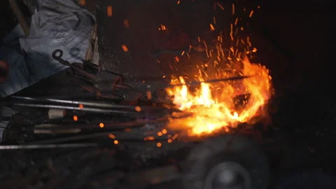 A blacksmith on fire heats the metal for forging the product Stock Footage 147005230
