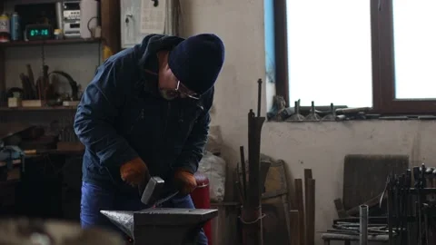 Blacksmith forges and makes metal detail with hammer and anvil at forge Stock Footage 168970829