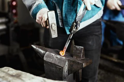 Blacksmith forges hinge on a anvil. Hammering hot red steel Stock Photos