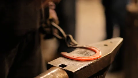 Blacksmith forges a horseshoe in a craft workshop. Horseshoe for good luck Stock Footage 98159012