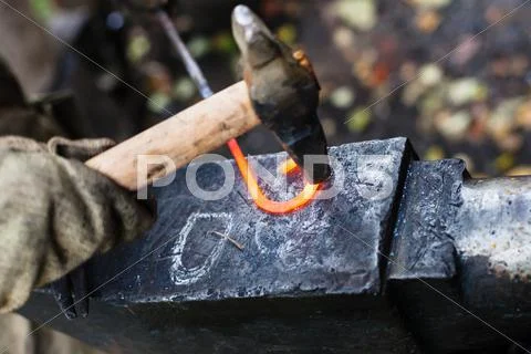Blacksmith forges iron buckle with hammer on anvil Stock Photos