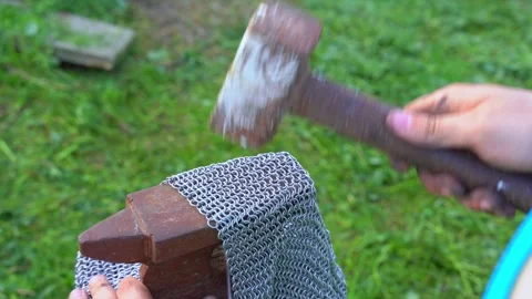 Blacksmith forges metal chain mail in village yard, hitting anvil with a hammer Stock Footage 276515686