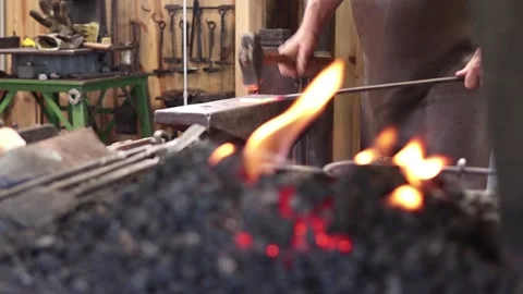 Blacksmith forging at the anvil looking across the forge fire, slow motion Stock Footage 133015344