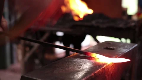 Blacksmith forging a bar of hot iron between hammer and anvil Stock Footage