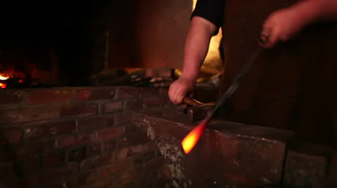 Blacksmith forging iron stops looks at work puts back in fire, medium shot Stock Footage 39016021