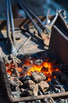Blacksmith furnace with burning coals, tools, and glowing hot metal workpiece Foto stock