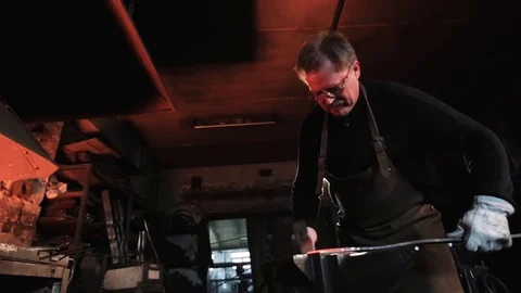 The blacksmith in glasses uses a hammer to forge metal Video stock 128522392
