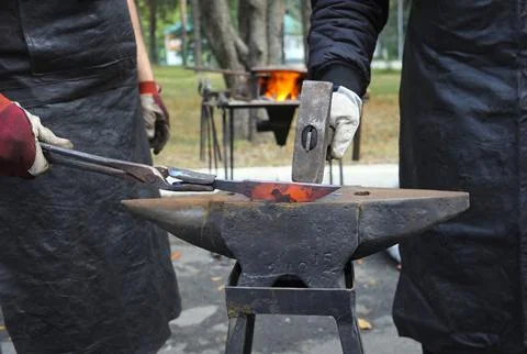 Blacksmith hands holding forceps and a hammer forging a metal billet blade of a Stock Photos