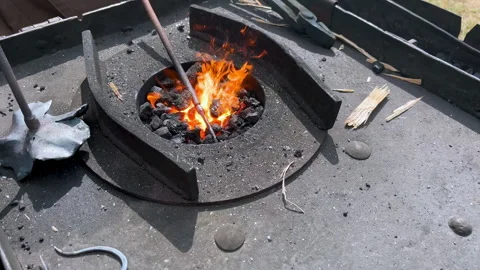 Blacksmith heating iron in a blazing coal forge, stirring hot embers with a rod Stock Footage 327392667