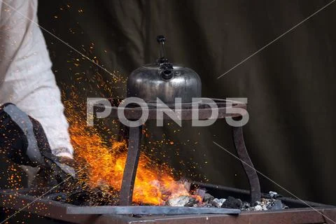 Blacksmith heating up metal in red hot coals while tea pot boiling water Stock Photos