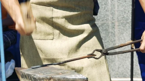 A Blacksmith Holding a Massive Hammer Banging Hot Metal Bar on Anvil. Stock-Footage 110836516