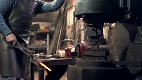 Blacksmith holding red hot iron bar working at large industrial hammer Stock Footage 132653117