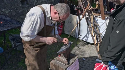 Blacksmith in linen shirt and apron forging iron at Easter festival. Stock Footage 332731111