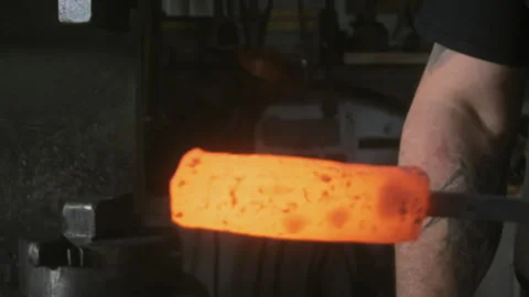Blacksmith lowering a piece of hot glowing metal in a forge Stock Footage 275509579