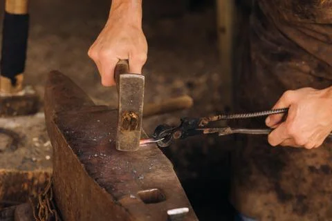 A blacksmith manually forges red-hot metal on an anvil with a hammer Stock Photos