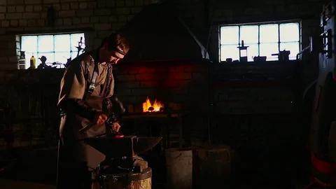 The blacksmith manually forging the molten metal on the anvil in smithy with Stock Footage 73971649