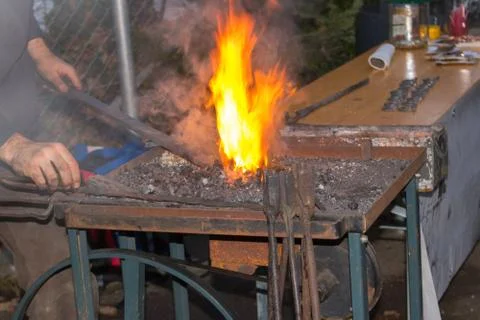 The blacksmith manually forging the molten metal on the anvil in smithy with Stock Photos