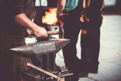 The blacksmith manually forging the molten metal on the anvil in smithy with Stock Photos