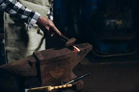 The blacksmith manually forging the red-hot metal on the anvil in smithy. Stock-Fotos